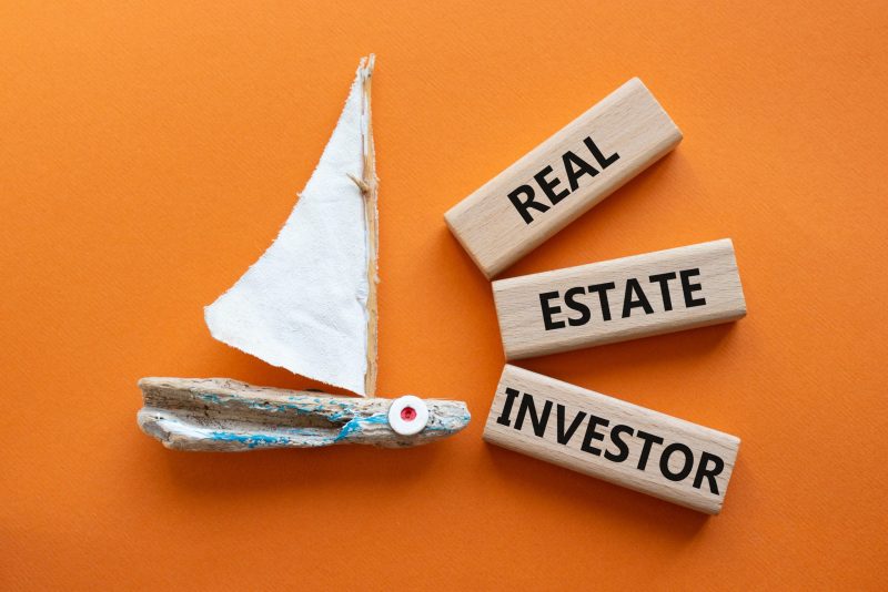 Real Estate Investor symbol. Wooden blocks with words Real Estate Investor. Beautiful orange background with boat. Business and Real Estate Investor concept. Copy space.