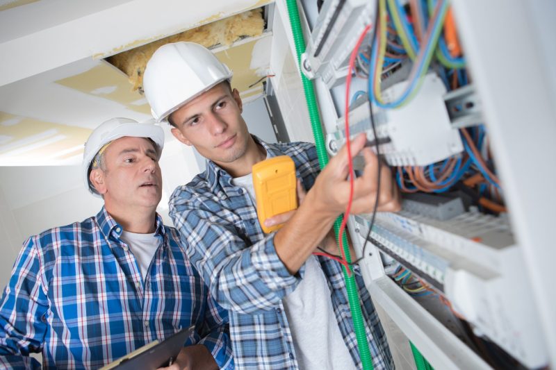 Trainee electrician working on fusebox under supervision