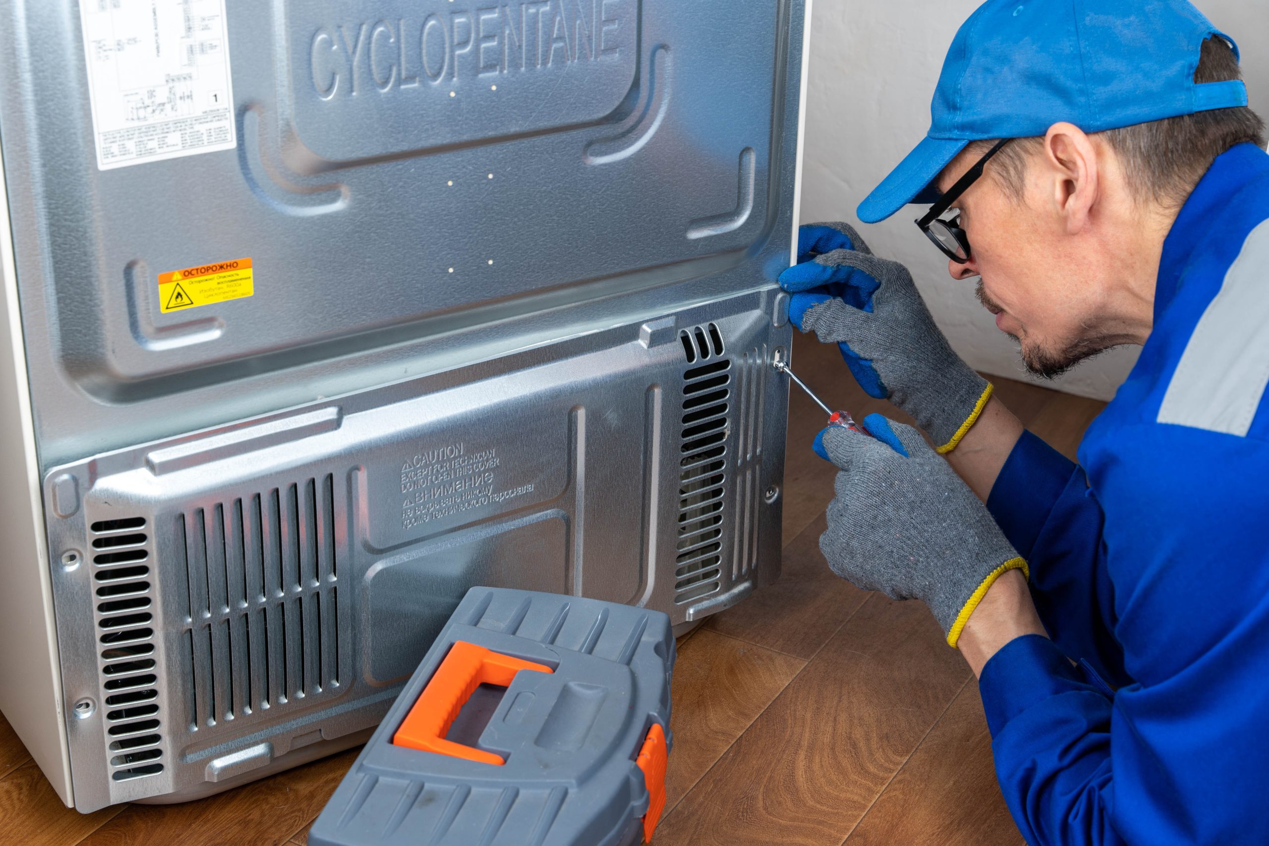 Repairing a refrigerator at home by a technician with blue gloves and tools